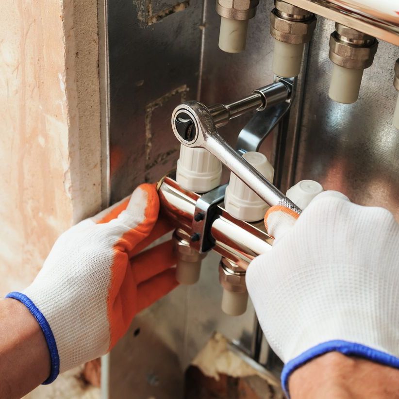 a person wearing gloves is working on a pipe with a wrench