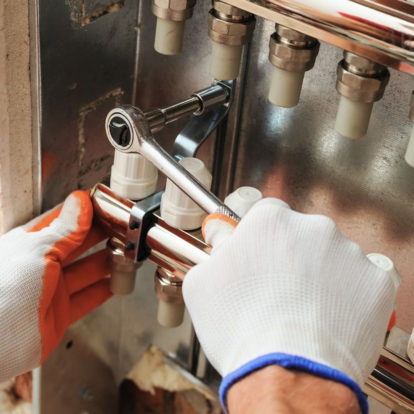 a person wearing orange gloves is working on a pipe with a wrench