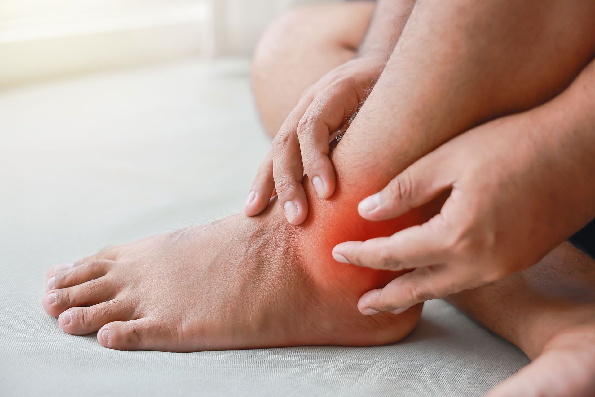 Hands holding an ankle, highlighting an area of inflamed, reddened skin.