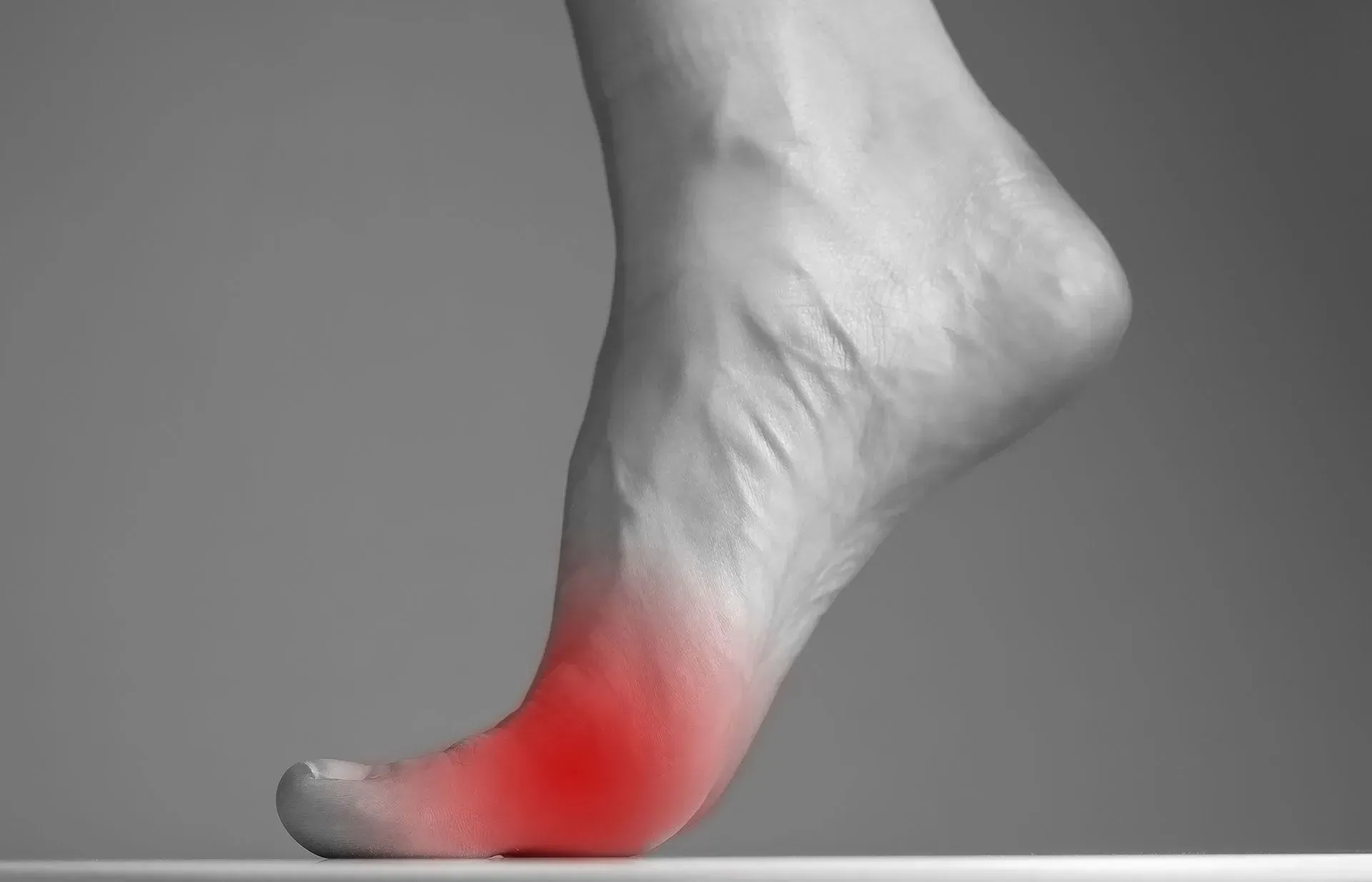 A side view of a human foot resting on its toes, with the ball of the foot highlighted in red to indicate pain.