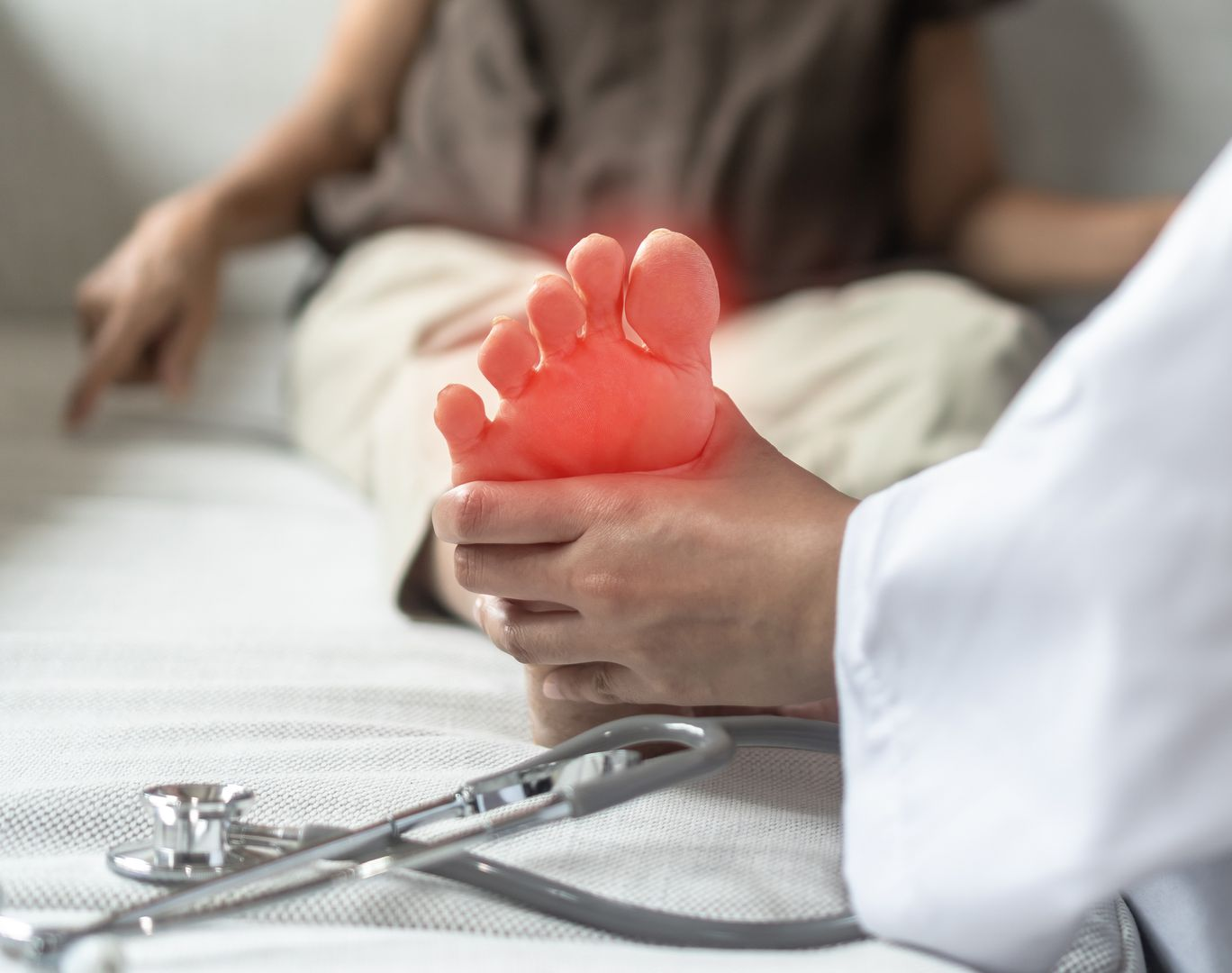 A medical professional examines a patient's foot, which is digitally highlighted in red to indicate pain or inflammation.