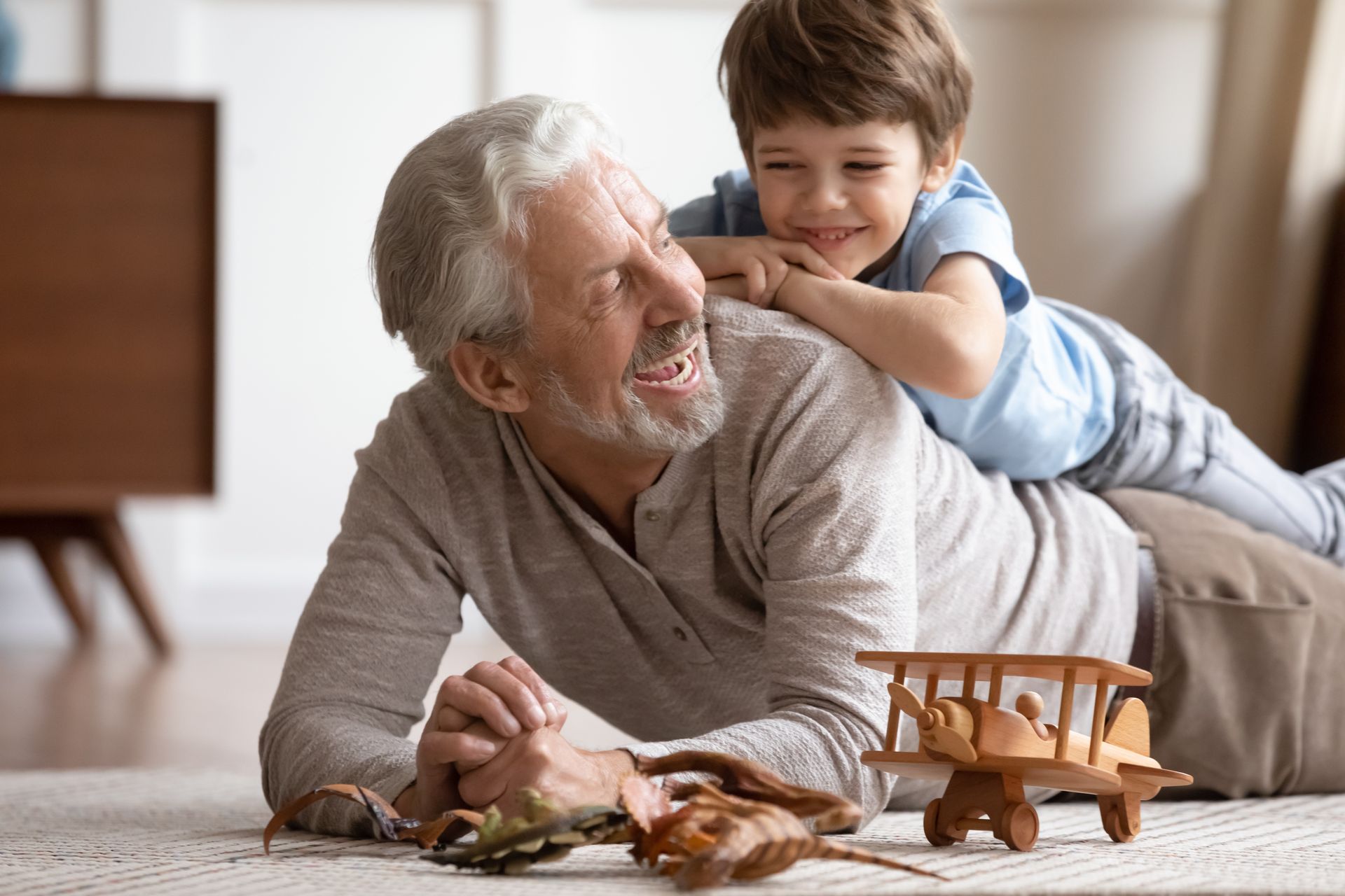 Grandfather and grandson smiling, playing on floor with wooden toys.