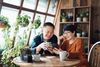 Smiling senior couple looking at a phone together at a table surrounded by plants; wood interior.