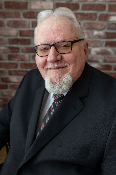 Man with glasses, graying hair, and goatee smiles, wearing a suit and tie.
