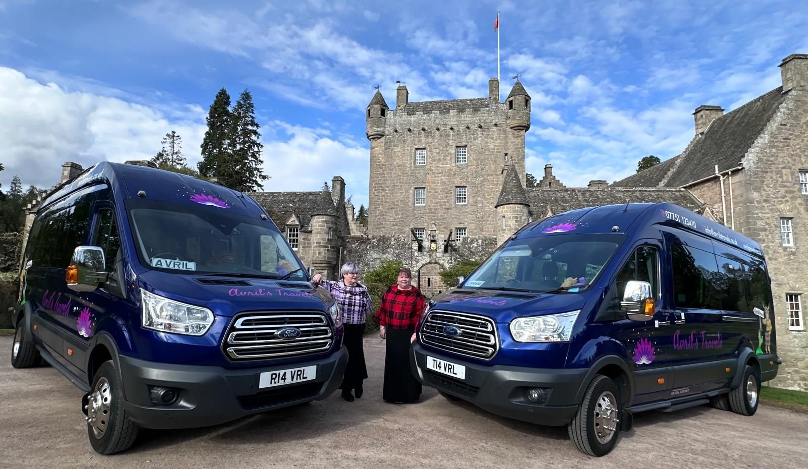 Two vans are parked in front of a castle.