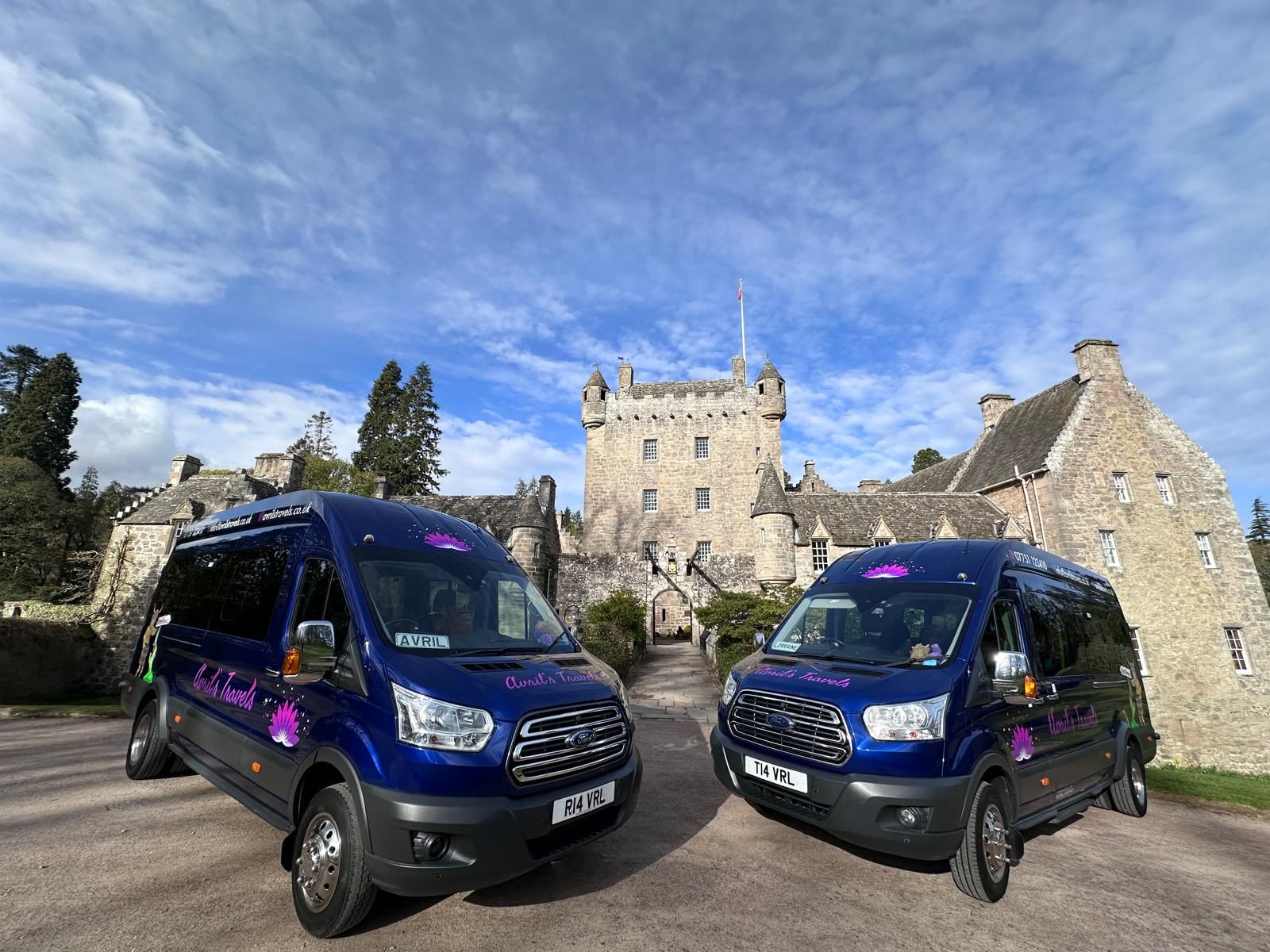 Two blue vans are parked in front of a castle.