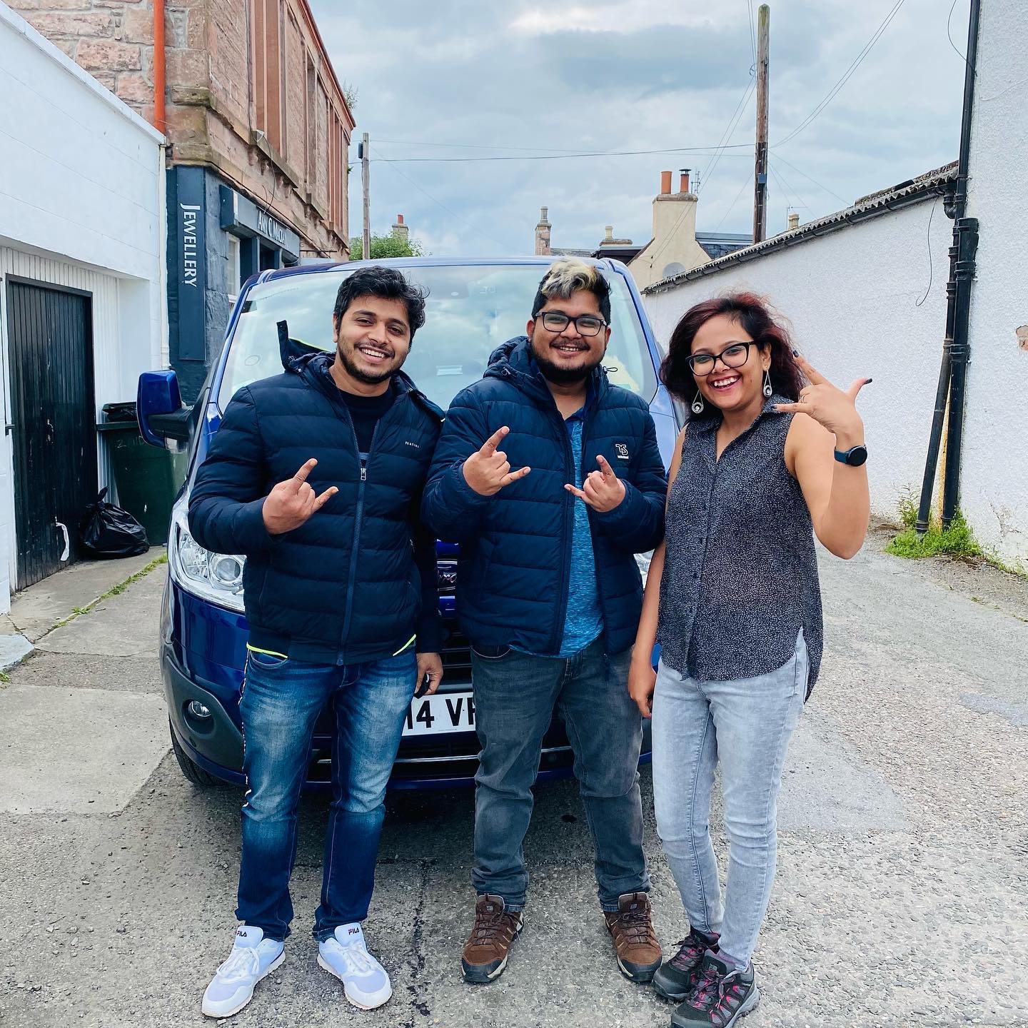 Three people are posing for a picture in front of a car.