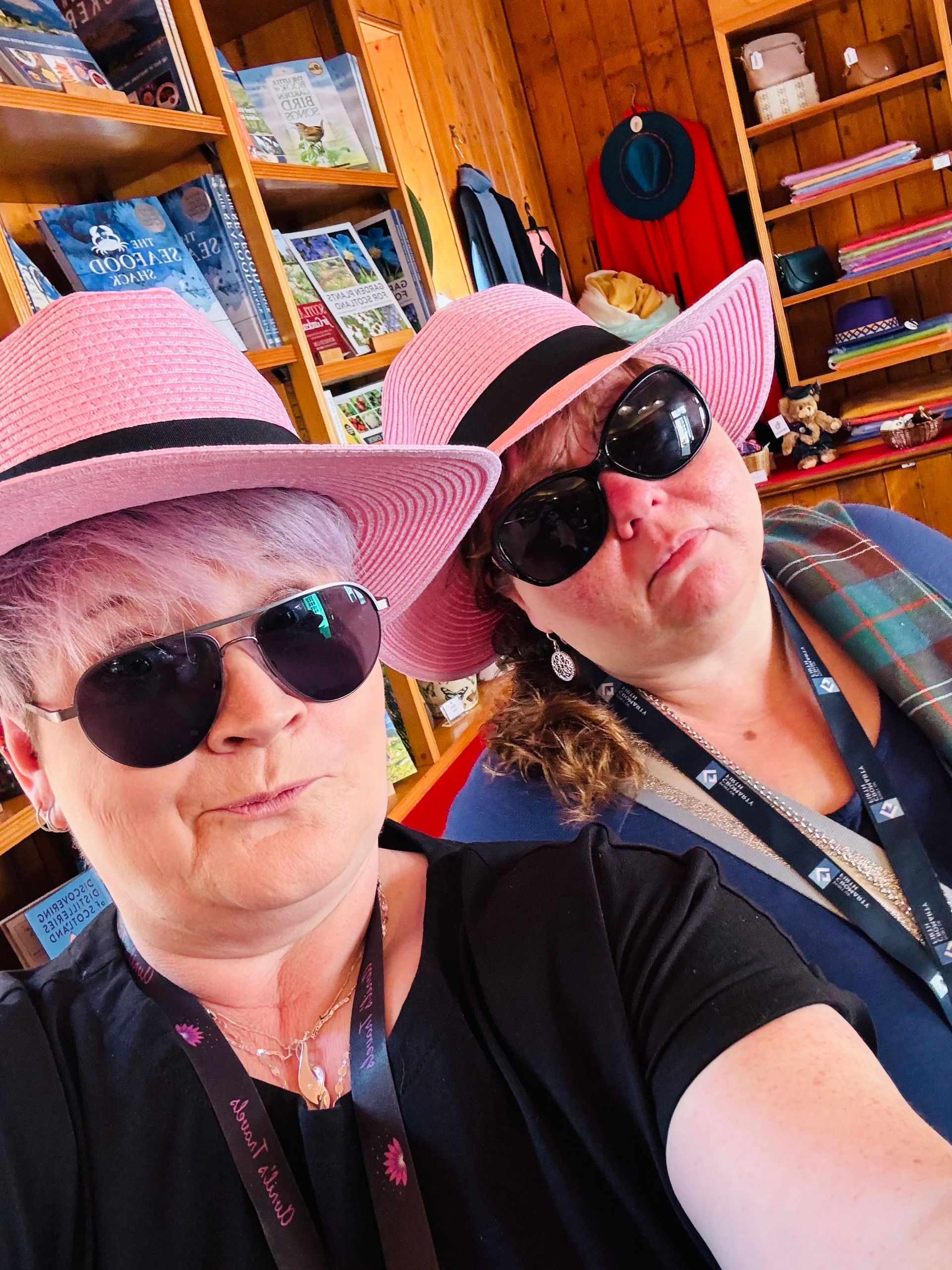 Two women wearing pink hats and sunglasses are taking a selfie in a store.