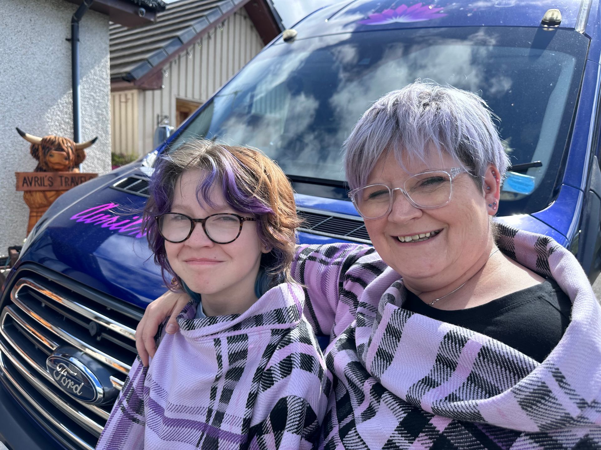 A mother and daughter are posing for a picture in front of a blue van.