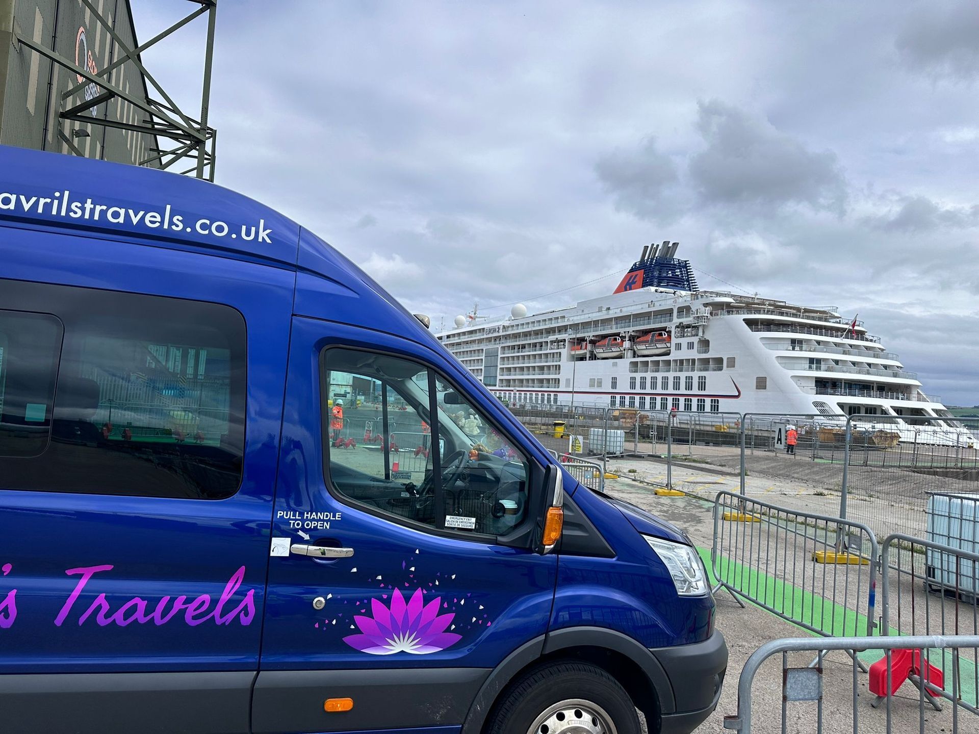 A blue van is parked in front of a large cruise ship.