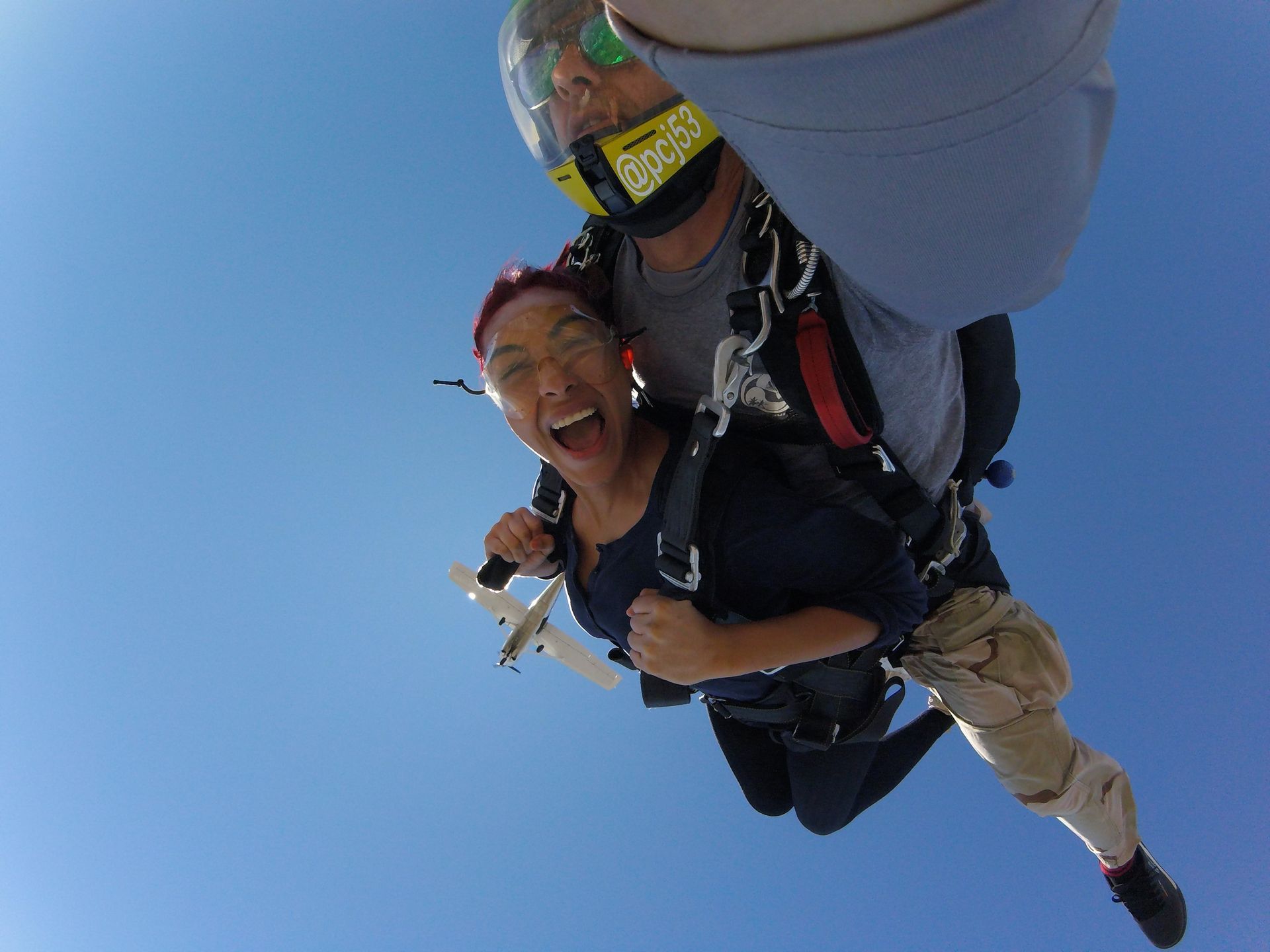 A tandem skydive pair freefall after exiting an airplane and take a selfie in the air.