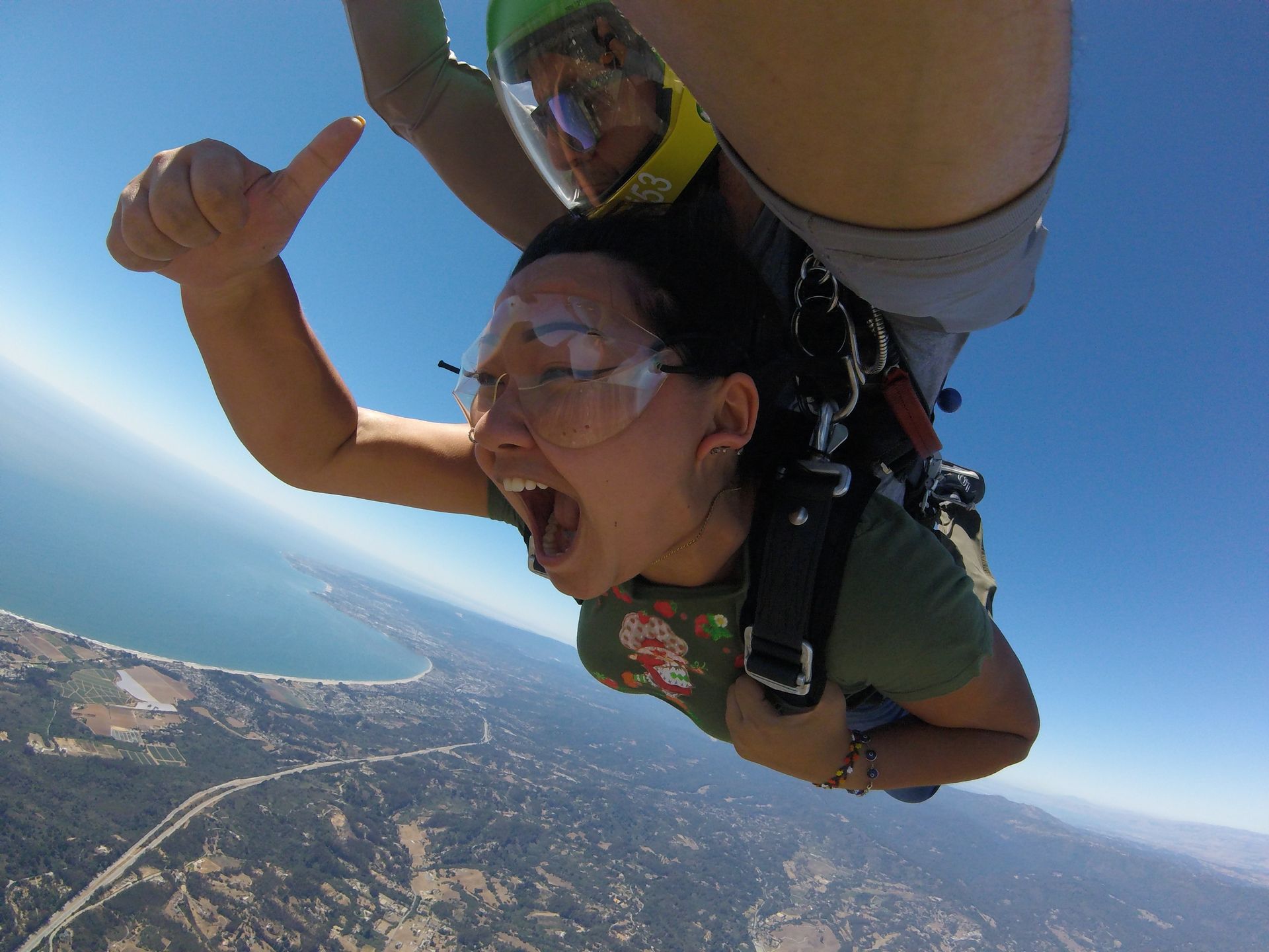 A woman is giving a thumbs up while freefalling through the air near Skydive Santa Cruz. 