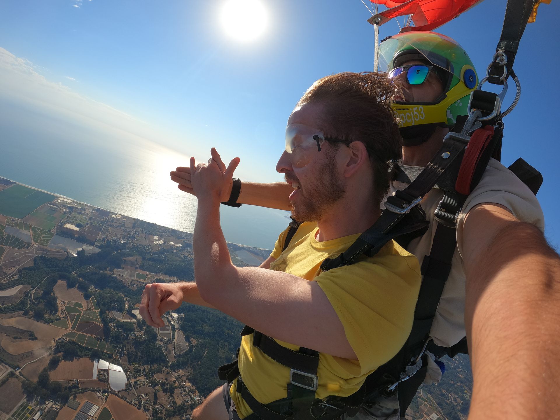 Skydive student man in a yellow shirt high fives instructor during parachute descent over Watsonville Airport.