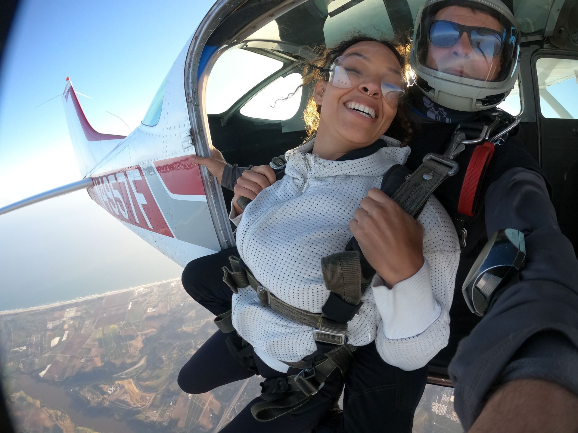 Tandem skydive student and instructor smiling while sitting on the edge of airplane.