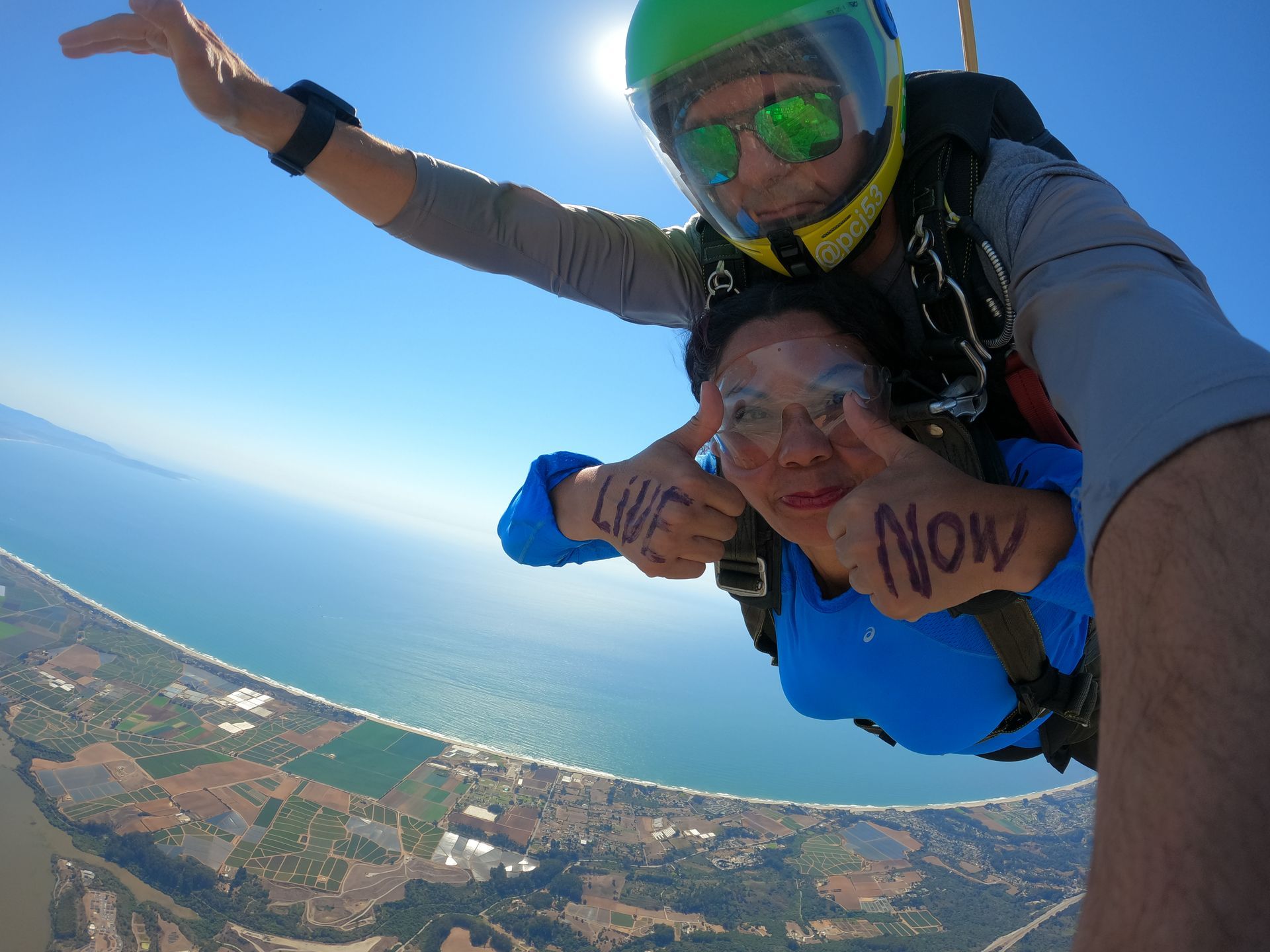 Tandem skydiving pair freefalling near the Pacific ocean in Santa Cruz. Woman has the words 