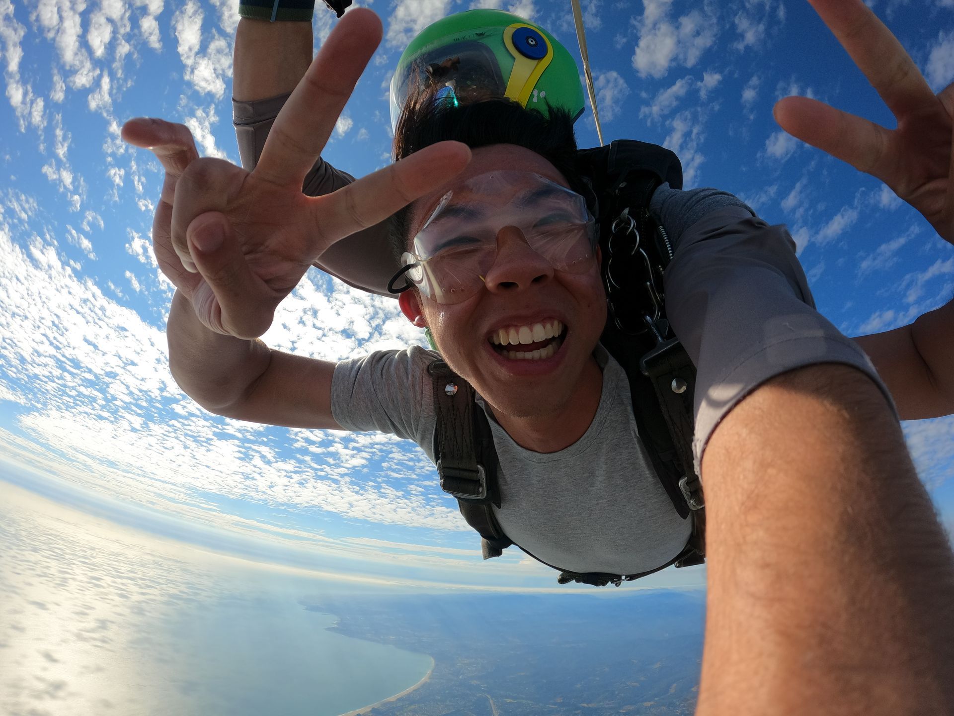 A male tandem student wearing goggles is making a peace sign in the air during freefall at Skydive Santa Cruz. 