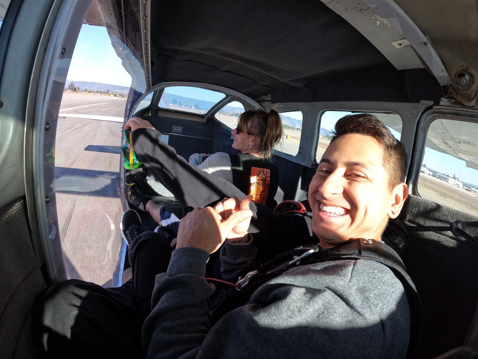 A man is smiling while sitting in the front of the Skydive Santa Cruz plane during takeoff.