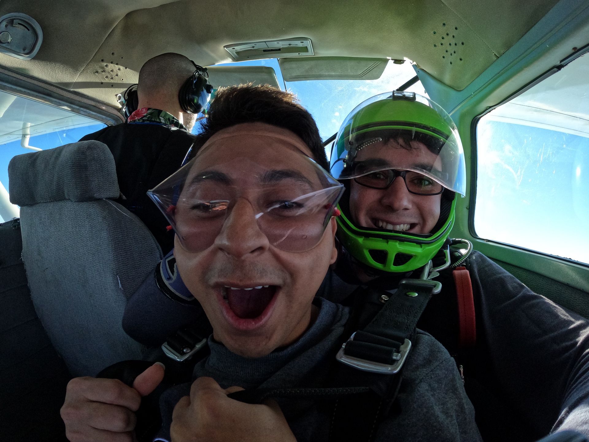 Tandem skydive student is stoked in skydive airplane just prior to jumping as instructor looks on happily. 