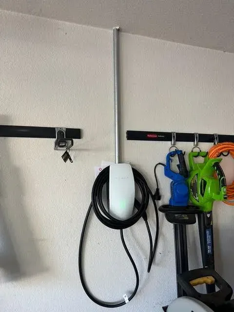 Tesla electric car charger mounted on a garage wall with a black cable and a hanging cord.