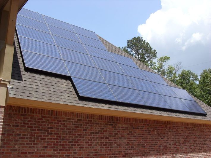 Solar panels on a brick home's roof, blue against a sky with clouds.
