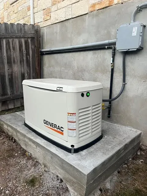 A Generac generator on a concrete pad next to a building with electrical conduit and a fence.