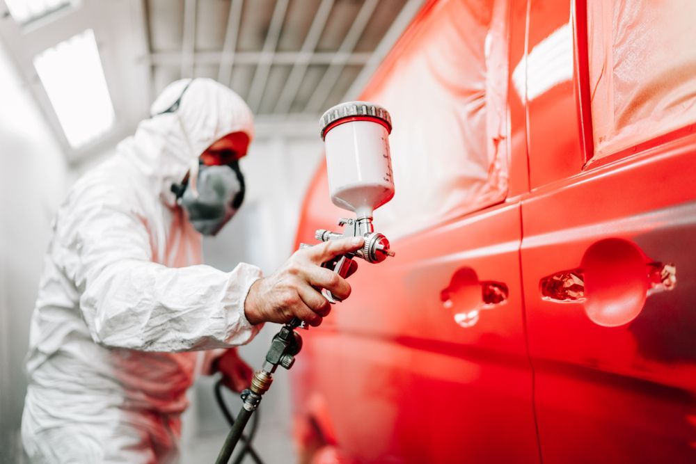 A Man in a Protective Suit is Spray Painting a Red Van — T & C Smash Repairs In Coffs Harbour, NSW