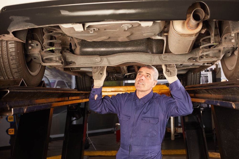 A Man is Working Under a Car on a Lift in a Garage — T & C Smash Repairs In Coffs Harbour, NSW