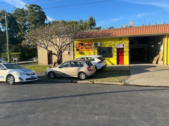 A Yellow Building With a Red Door and a Garage, Cars Parked in Front — T & C Smash Repairs In Coffs Harbour, NSW