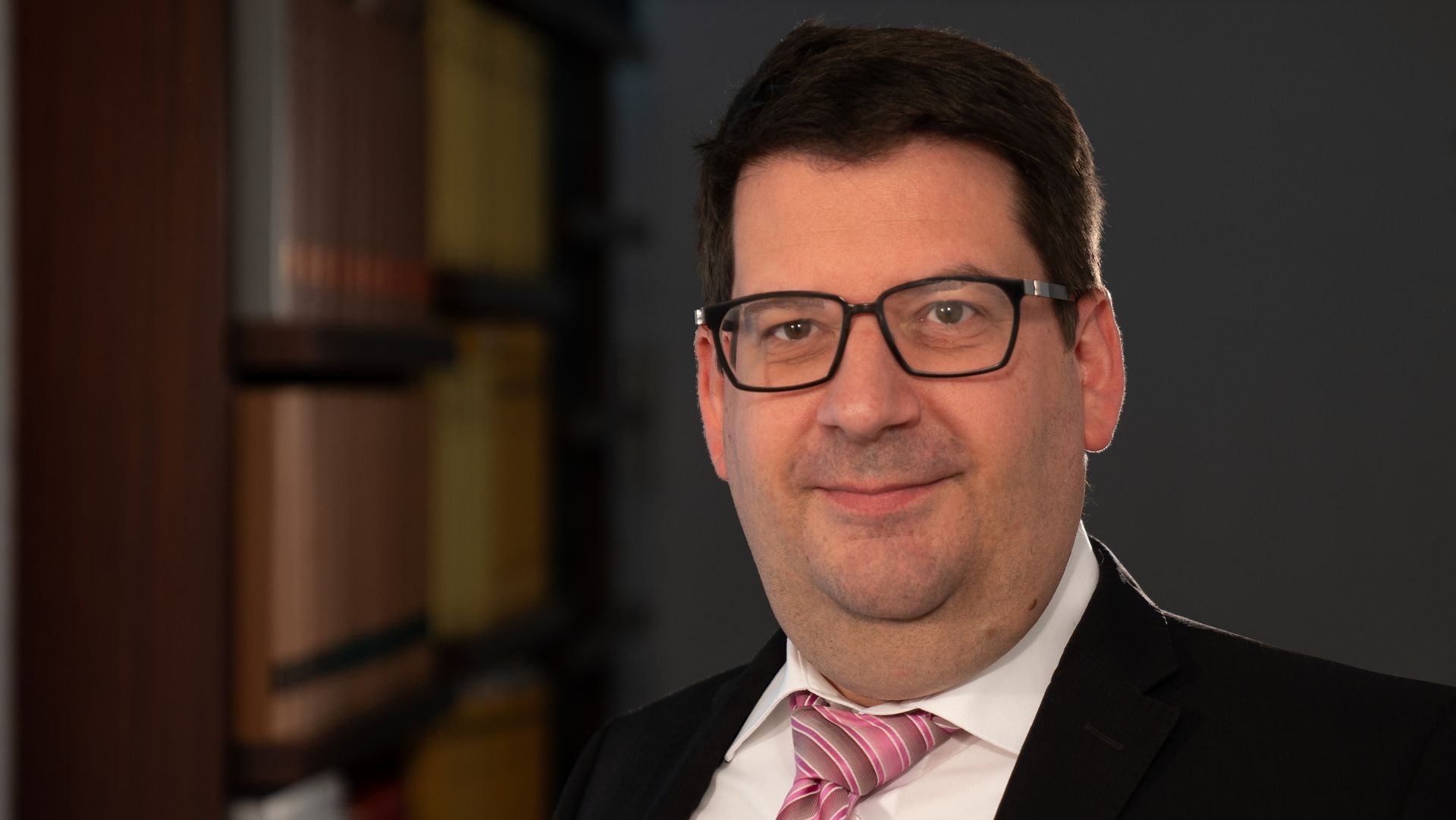 Ein Mann in Anzug und Krawatte lächelt in die Kamera.