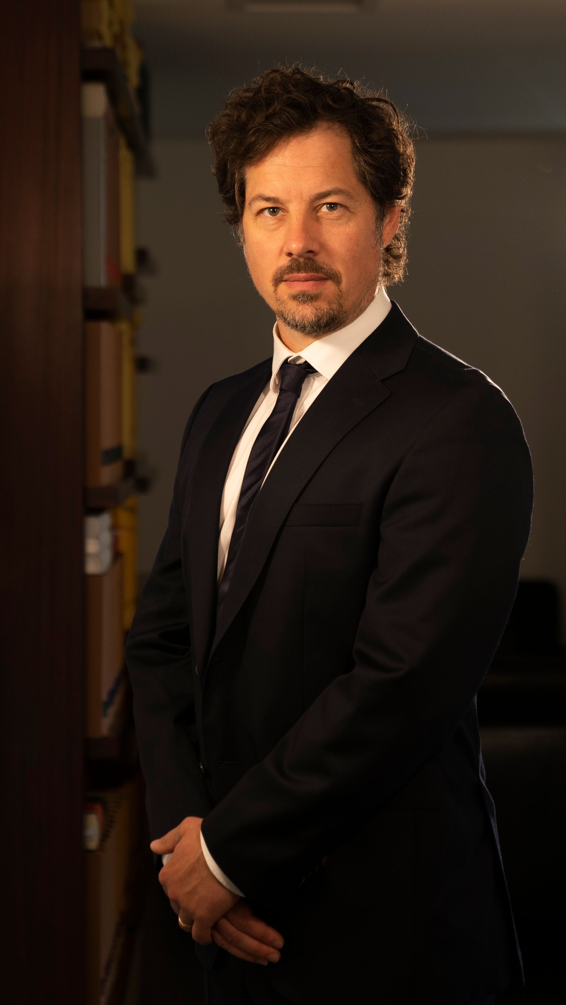 A man in a suit and tie is standing in front of a bookshelf.