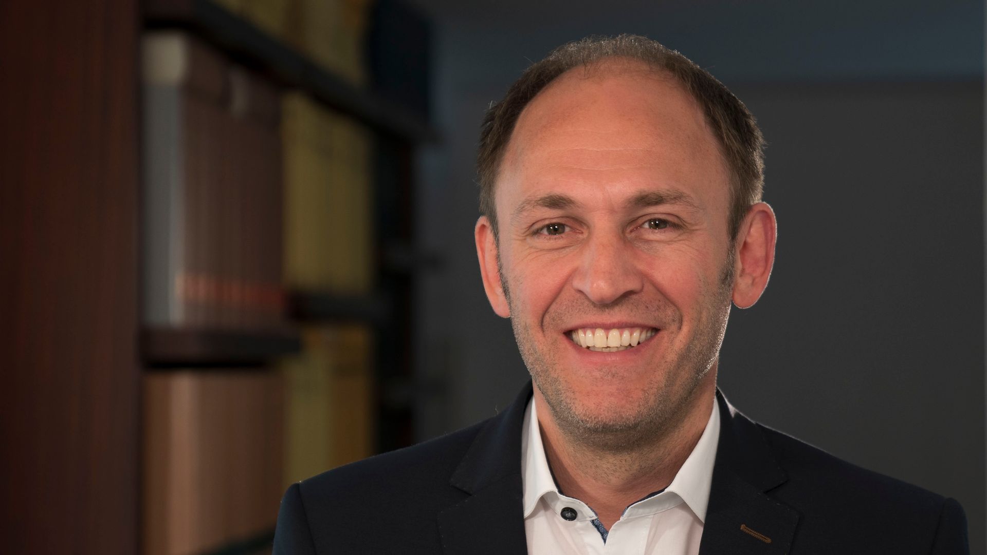 Ein Mann in Anzug und weißem Hemd lächelt in die Kamera.