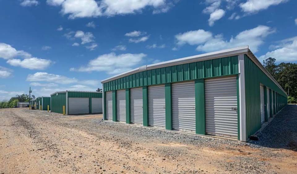 A row of green buildings with white doors on a dirt road.