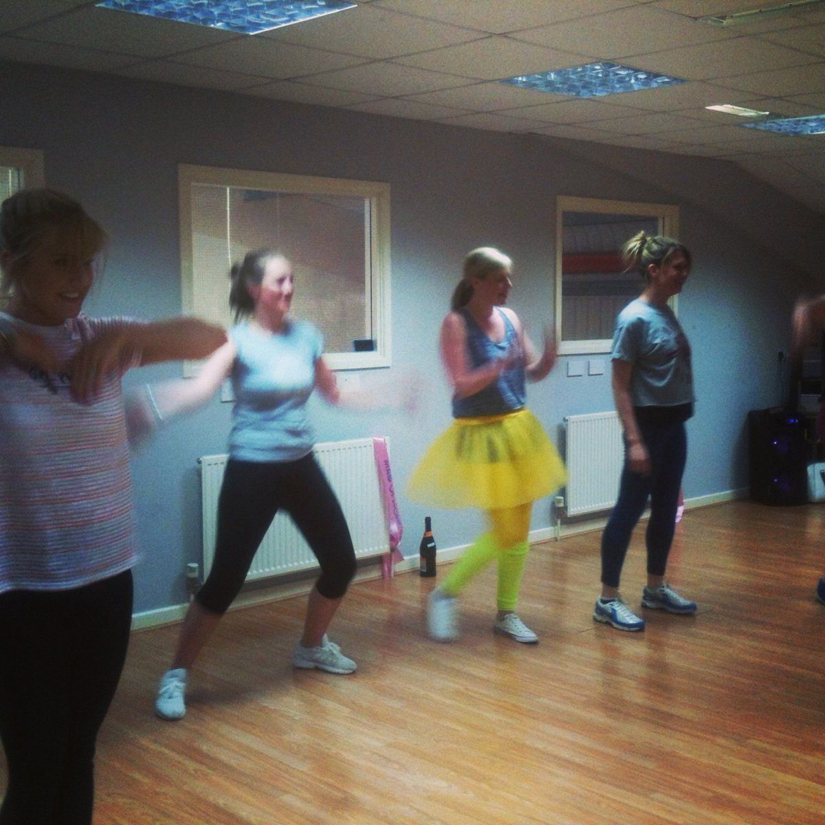 Group of women dancing in bright 80s outfits at an 80s Fame themed hen party dance class, enjoying a fun retro routine in a studio