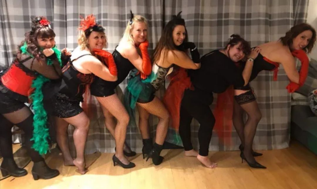 Hen group dressed in glamorous burlesque-style outfits striking fun poses inside the dance studio