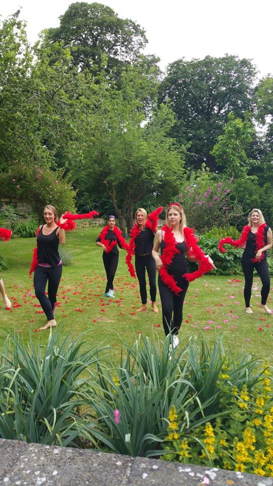 Hen party group dancing outdoors with red feather boas and lots of laughter during a burlesque-style dance session