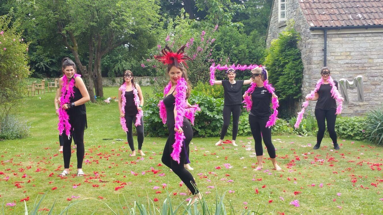 Hen party group performing a burlesque-style routine outdoors surrounded by greenery and flowers