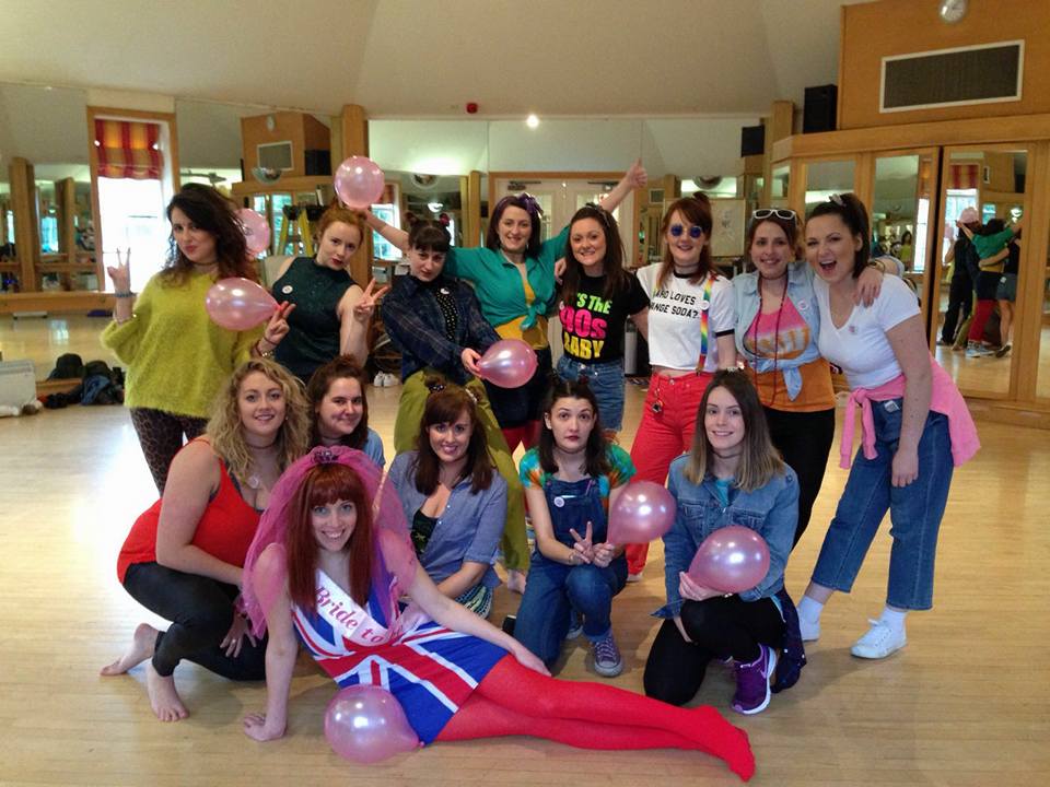 Group of women dressed in 90s outfits at a Spice Girls themed hen party dance class, posing with balloons in a fun studio setting