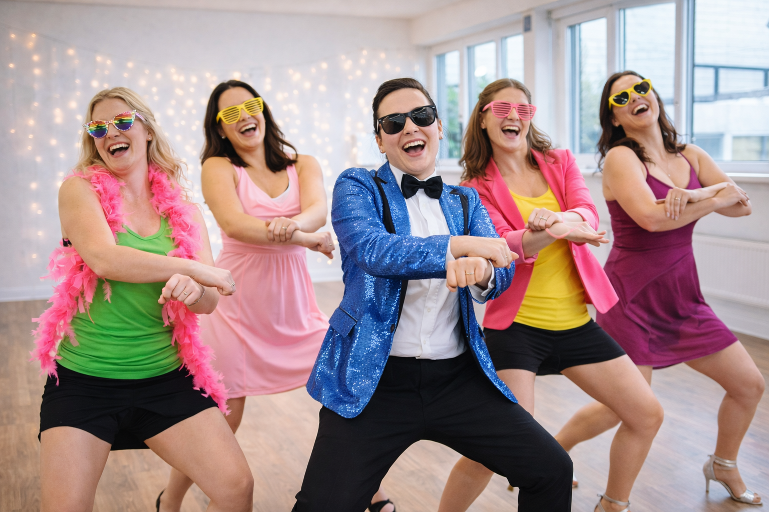 Group of women at a Gangnam Style hen party dance class in a studio, wearing fun outfits and sunglasses while performing the iconic dance move together