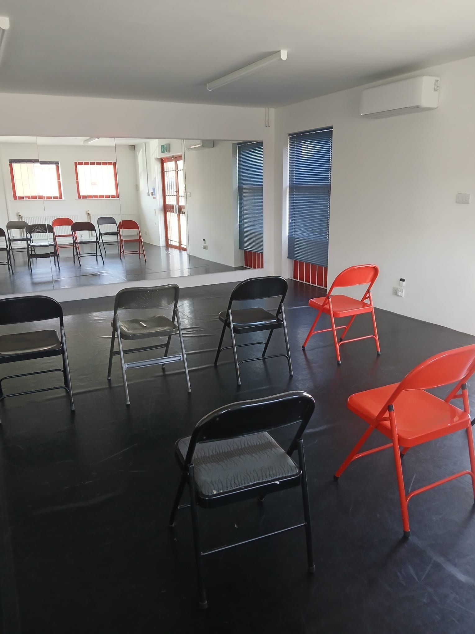 Studio space prepared for a chair dance workshop, with folding chairs spaced out on a black dance floor facing a full mirrored wall