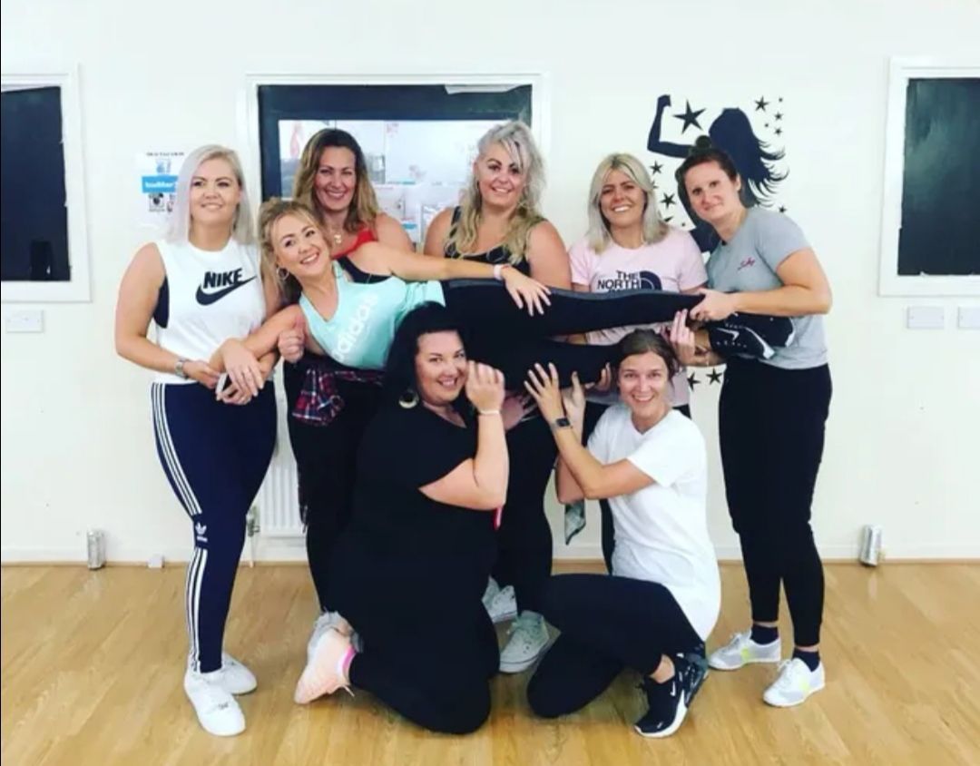 Hen party group laughing and posing in colourful costumes during a lively indoor dance class