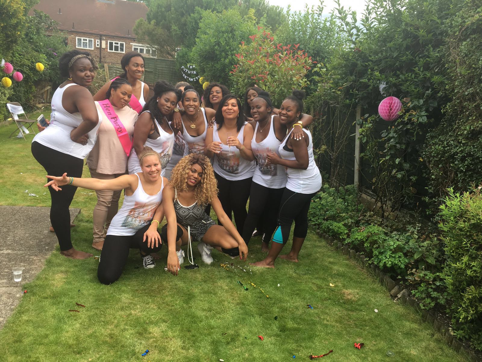 Group of women posing together at a twerk themed hen party dance class, celebrating outdoors in a garden setting