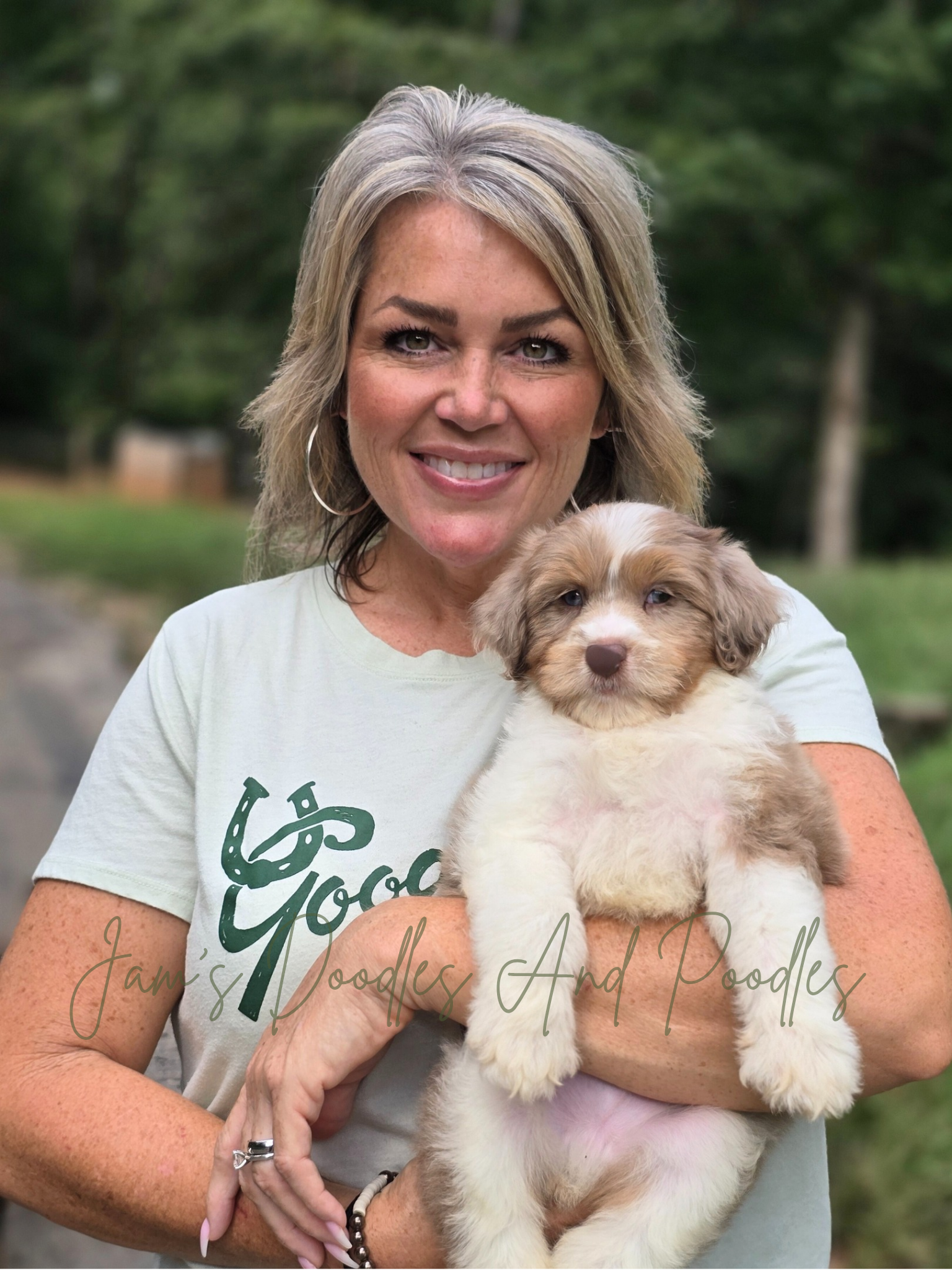 Woman holding a small, brown and white puppy, smiling outdoors.