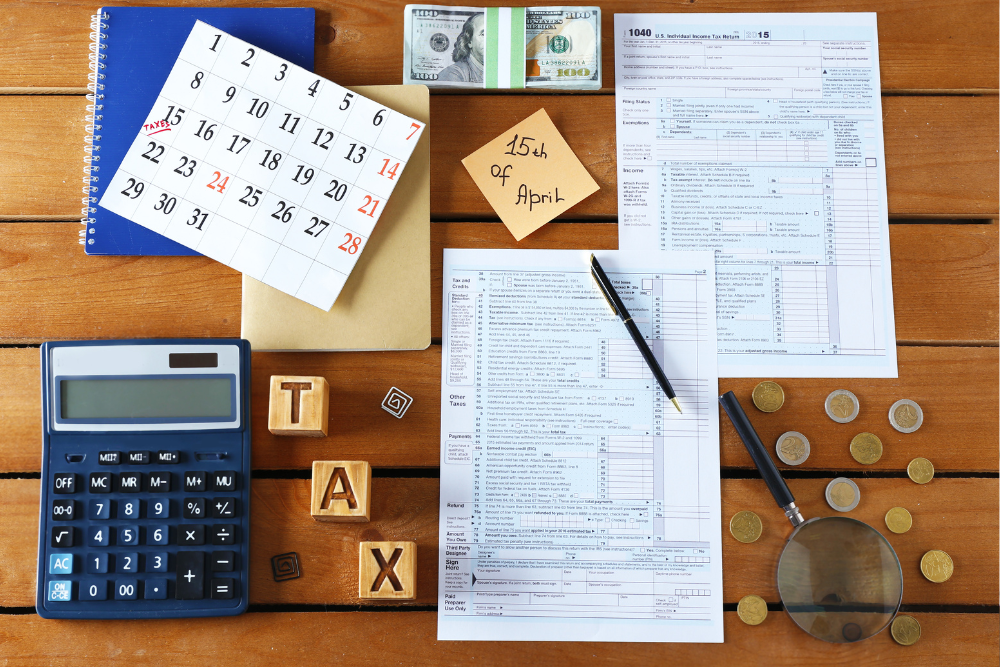A wooden table topped with a calendar , calculator , papers , coins and a magnifying glass.