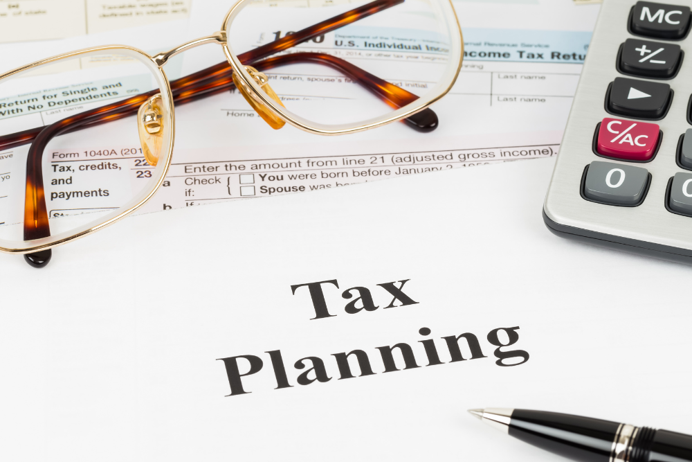 A pair of glasses , a pen , and a calculator are on a piece of paper that says tax planning.