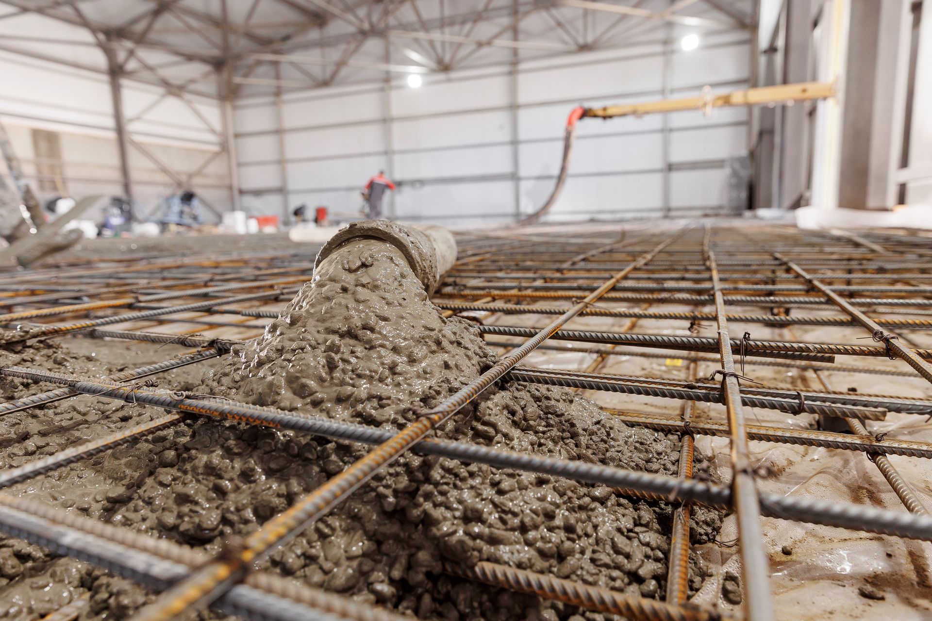 Concrete being poured onto a rebar grid in an industrial building, with a hose dispensing the mixture.