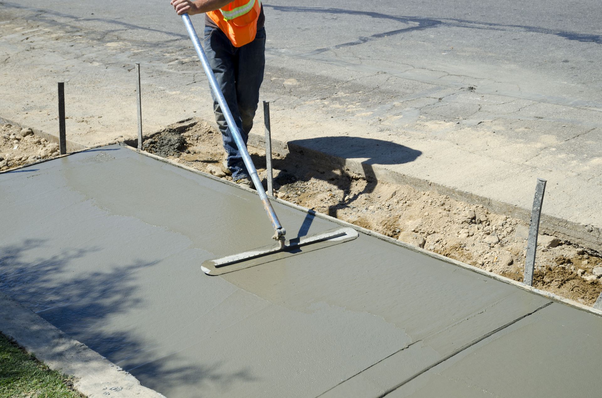 Person in safety vest leveling wet concrete sidewalk with a screed.