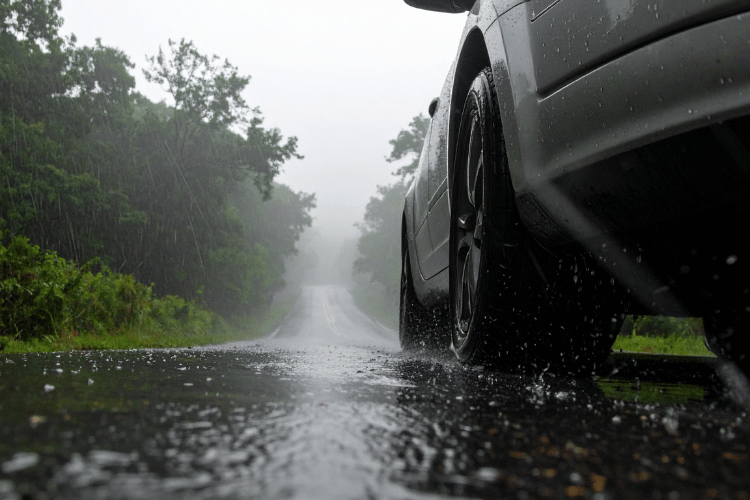 Close-up of a car tire driving on a wet road in heavy rain with water splashing.