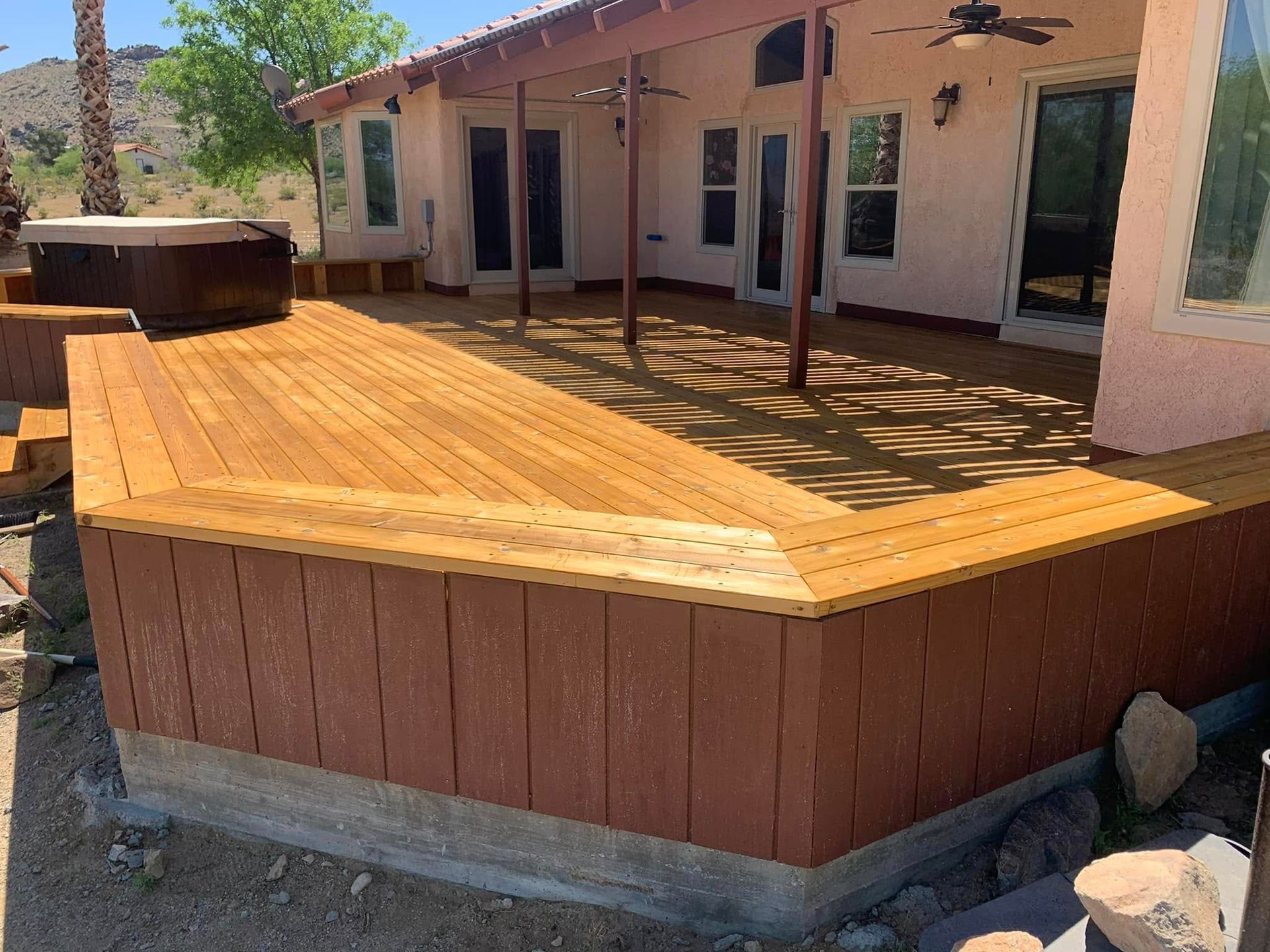 Wooden deck with hot tub, brown siding, and patio roof.