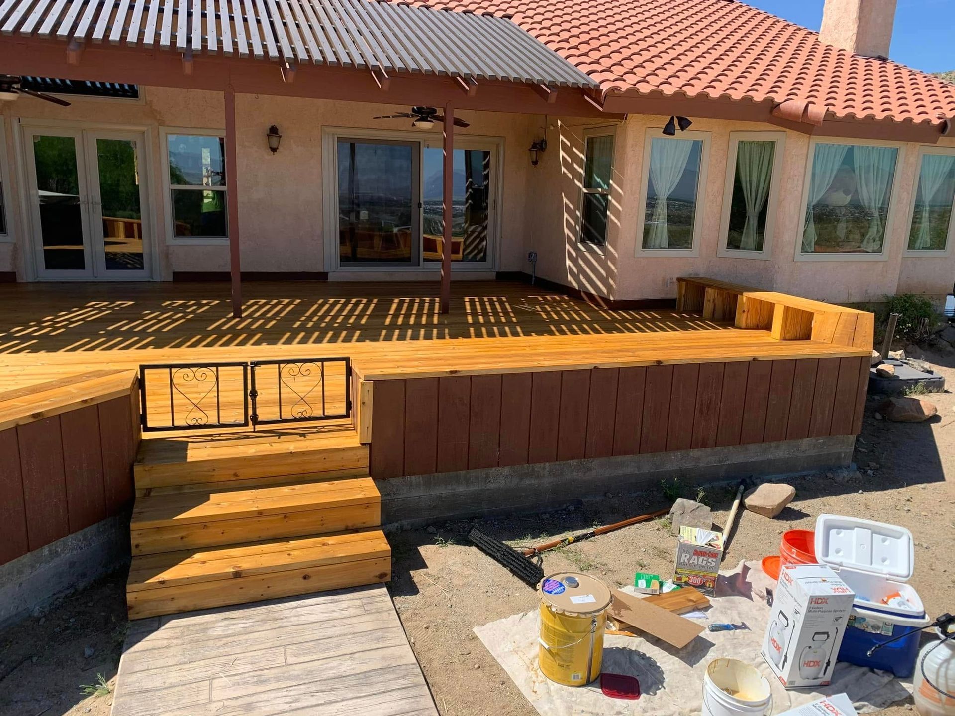 Wooden deck with stairs, built-in seating, and a house with a tiled roof.