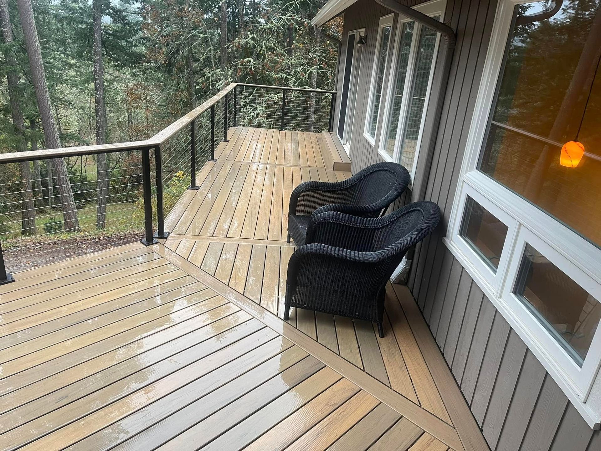 Wooden deck with two black wicker chairs. Forest view.